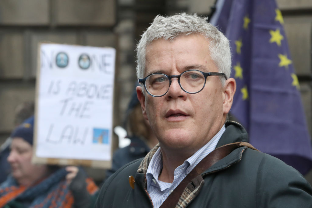 Jolyon Maugham standing outside the court of Session in Edinburgh. In the background is an EU flag and a woman holding a placard which reads "Noone is above the law"