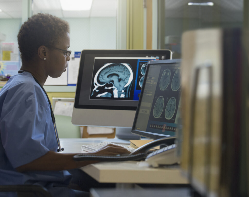 A female doctor sits at a desk looking at x-rays on two screens