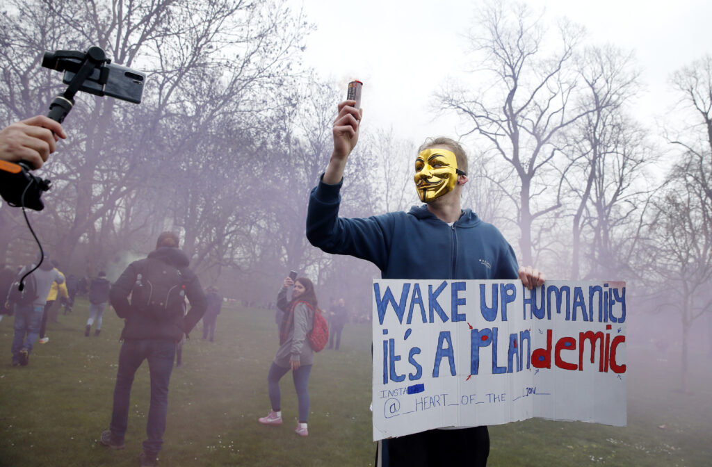A protester wearing a QANon mask poses with a flare and a sign calling for people to "wake up" during a protest in London