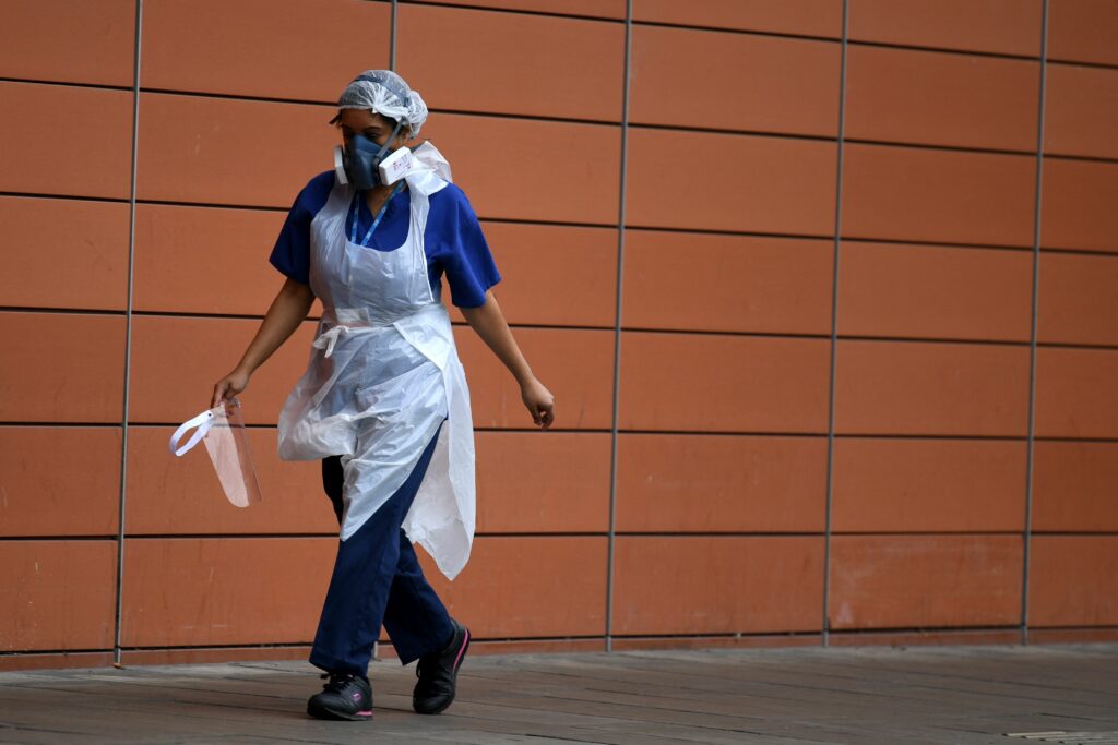 A nurse wearing protective face mask and apron walks outside a hospital