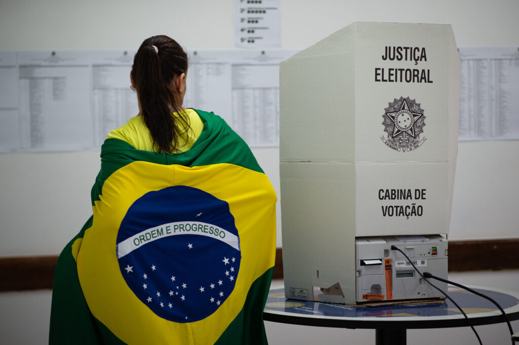 A woman wrapped in the Brazilian flag stands next to a polling booth